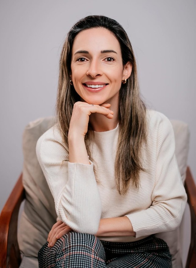 Chelin Caumo sorrindo, sentada em uma poltrona, de blusa clara